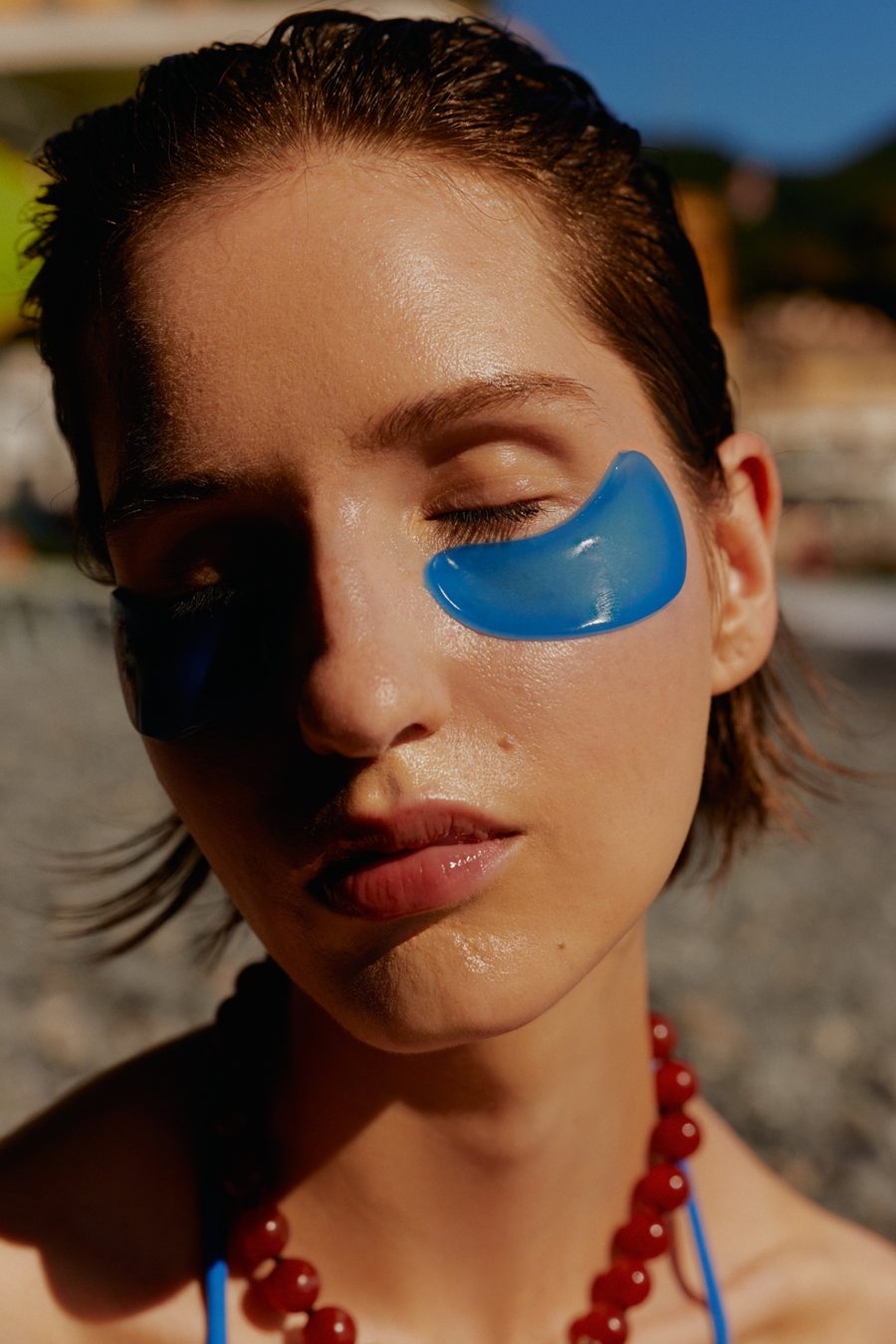 Close-up of a woman with her eyes closed and a blue eye patch, in bright sun
