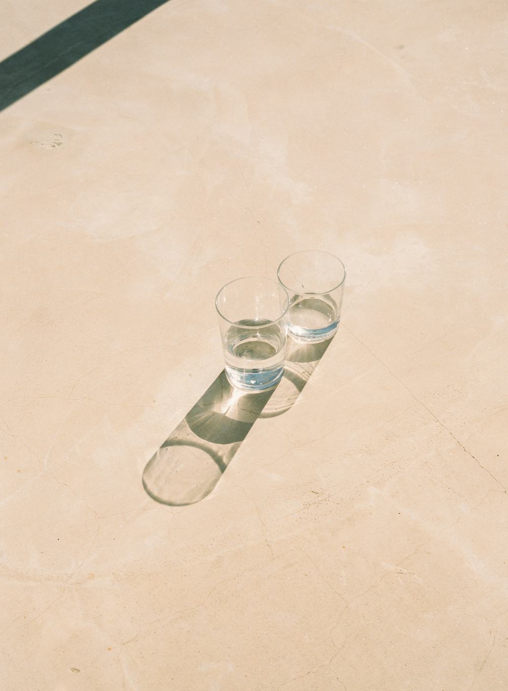 Two glasses of water casting long shadows on pale stone