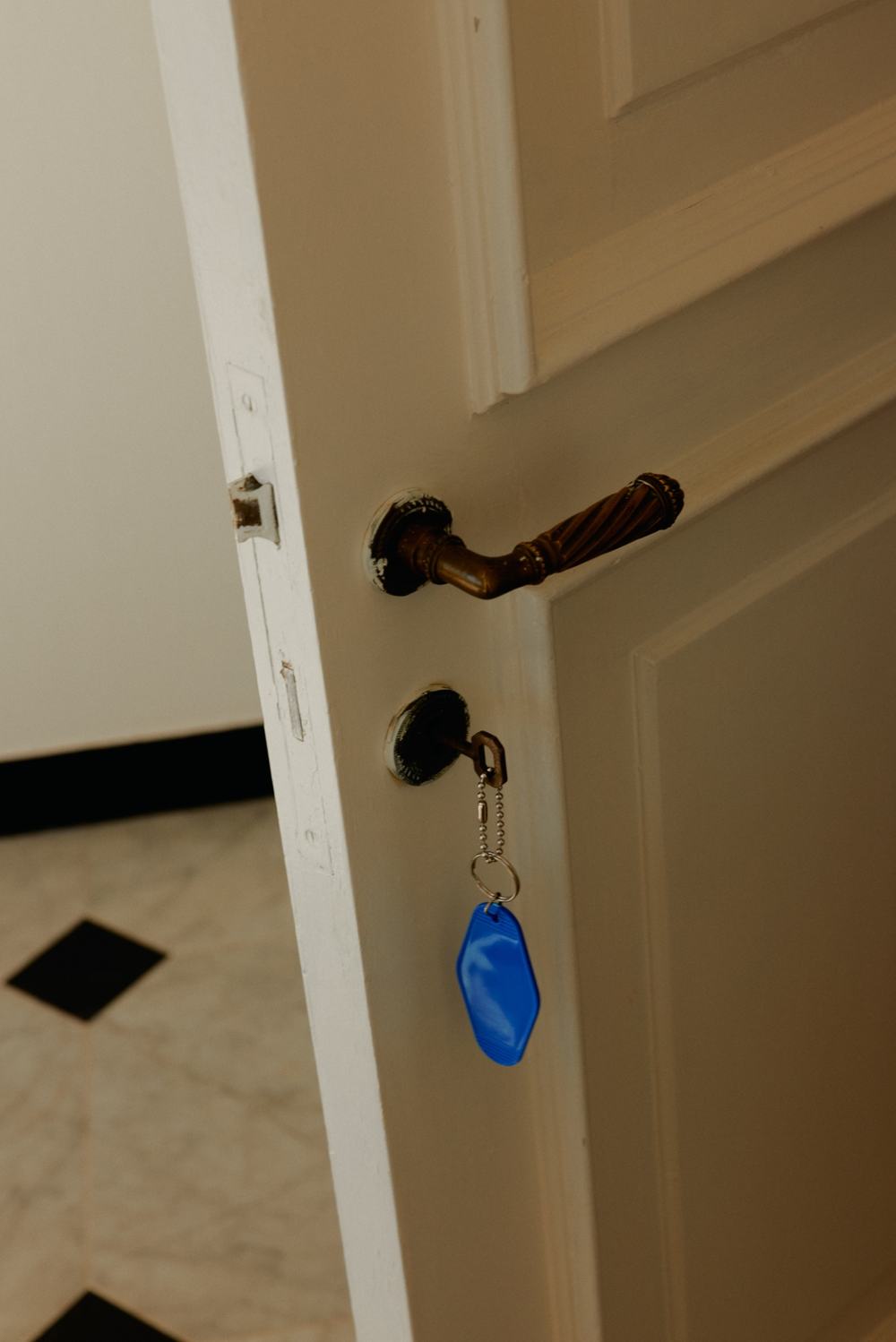 Brass door handle with a blue key tag hanging from the lock of an open white door