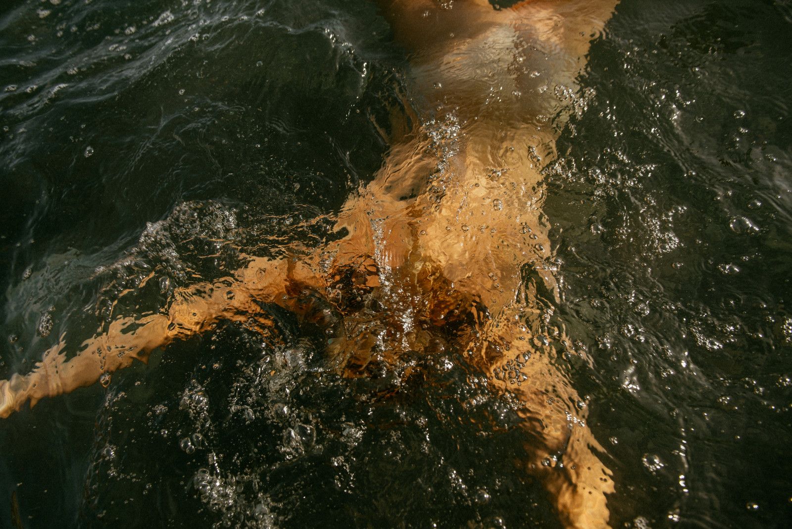 A swimmer seen from above, gliding under dark water in golden light
